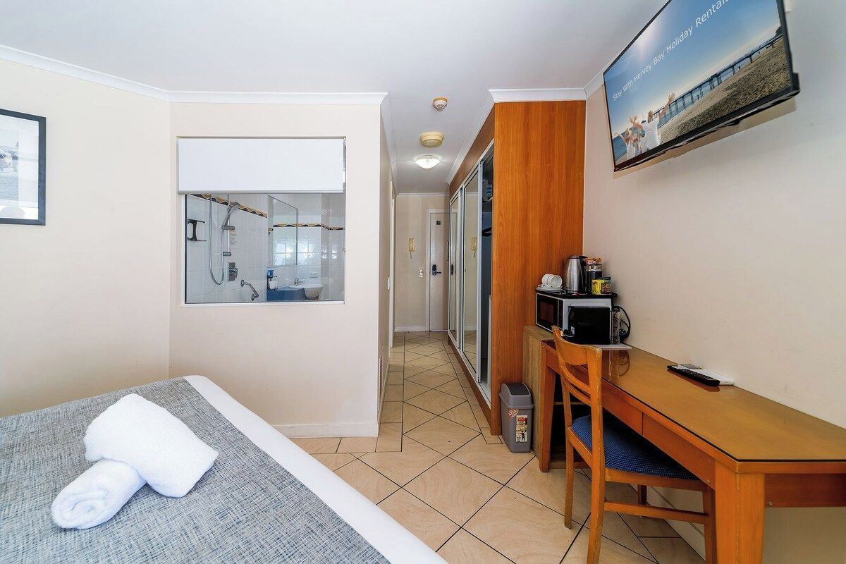 A hotel room with a bed, a desk, a television, and a bathroom with a shower.