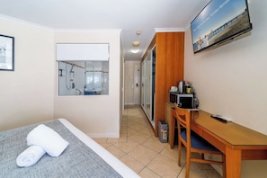 A hotel room with a bed, a desk, a television, and a bathroom with a shower. - Mantra Top Floor Hotel Room (Urangan)