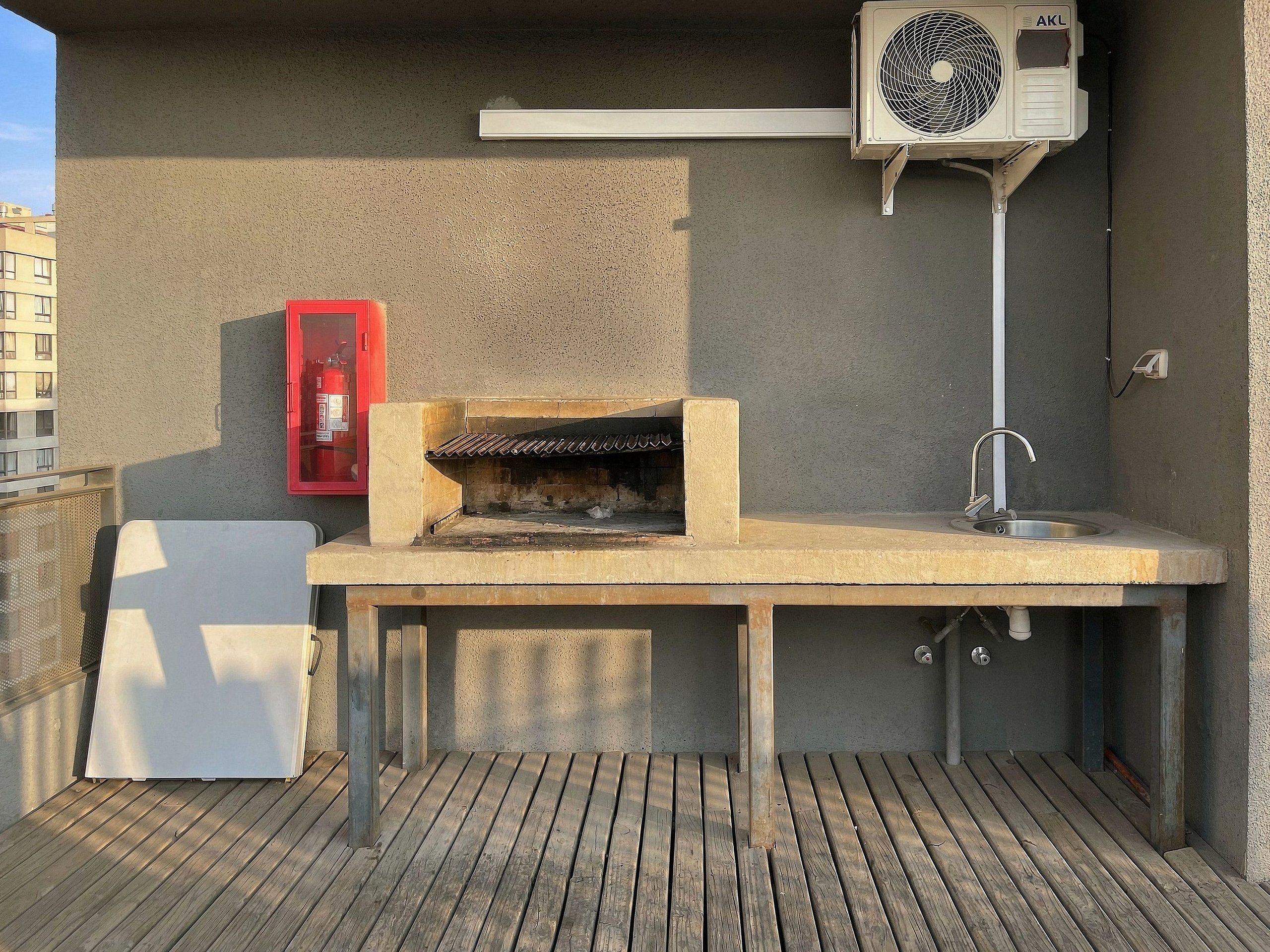 Een buitenkeuken met een ingebouwde barbecue, een spoelbak en een airconditioning.