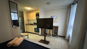 A hotel room with a bed, a desk, a chair, a TV, and a kitchenette in the background. - Oceana Suites Edificio Hipódromo  (Región Metropolitana)