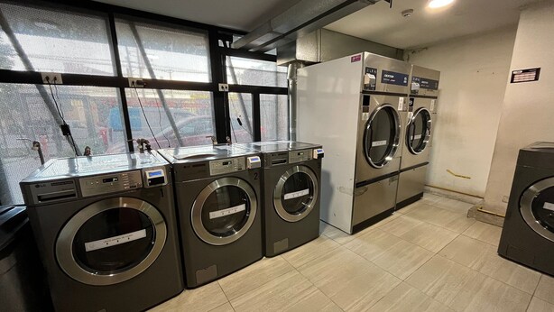 A laundry facility with multiple washing machines and dryers, a tiled floor, and a window with a view of the outside. - Oceana Suites Edificio Hipódromo  (Región Metropolitana)