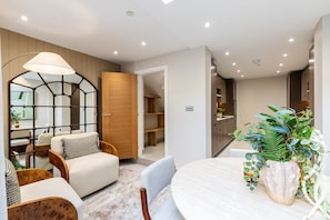 A modern interior with a dining area, a wooden door, and a kitchen visible in the background. - Luxury Three-Bed Chelsea Townhouse (London)