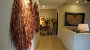 A hallway with a woven wall decoration, a table with a lamp, and a framed artwork on the wall. - Luxury penthouse with a private terrace and ocean views | Ayuuk (Cruz de Huanacaxtle)
