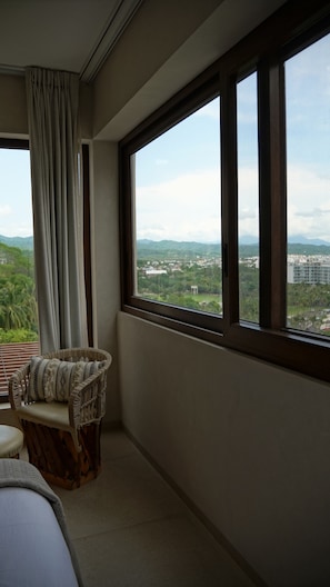A room with a large window, a wicker chair, and a view of a cityscape. - Luxury penthouse with a private terrace and ocean views | Ayuuk (Cruz de Huanacaxtle)