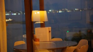A room with a table and chairs, a lamp, and a view of the cityscape through a window. - Luxury penthouse with a private terrace and ocean views | Ayuuk (Cruz de Huanacaxtle)