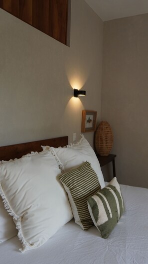 Ein Schlafzimmer mit einem Bett, Kissen, einer Wandlampe, einem Bilderrahmen und einem gewebten Korb.
