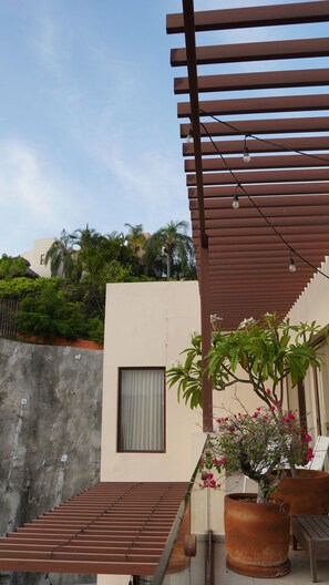 A balcony with a wooden pergola, potted plants, and a view of a residential area with palm trees.