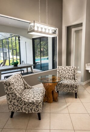 A modern room with a glass table and two patterned armchairs, a wooden coffee table, and a view of a swimming pool outside. - Luxury Home, Close to the Beach and Enclosed Pool. (Naples)