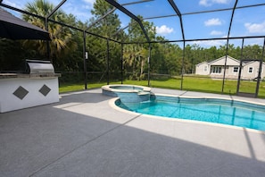 A swimming pool with a hot tub, surrounded by a covered patio with a grill, and a view of a residential area. - Luxury Home, Naples (Naples)