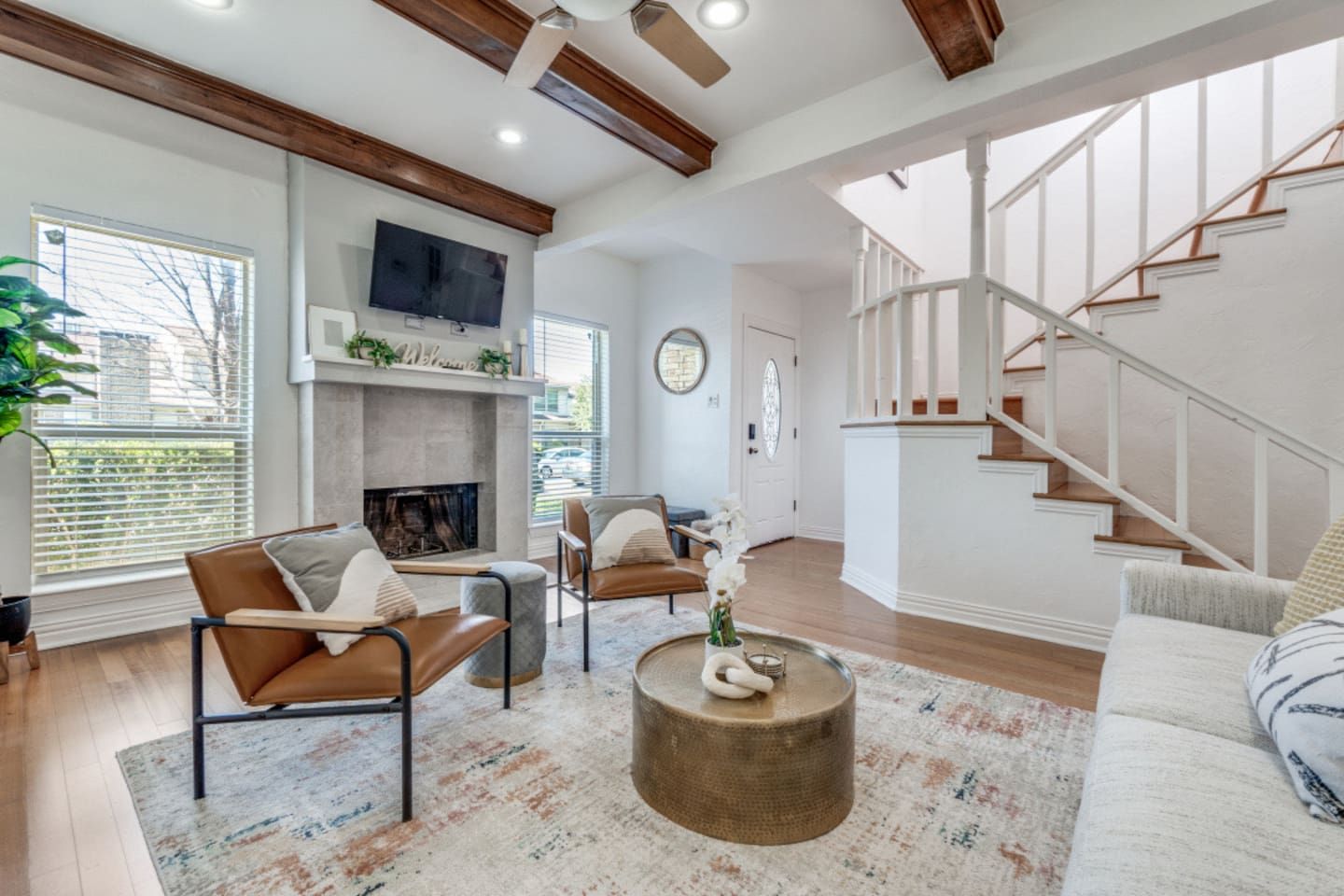 A spacious living room with a fireplace, a staircase, and a television mounted on the wall.