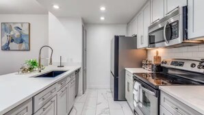 Een moderne keuken met witte kasten, roestvrijstalen apparatuur en een marmeren vloer.