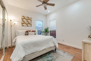 Ein Schlafzimmer mit einem Bett, einem Deckenventilator, einer Stehlampe, einem Wandbild und einem Fenster mit Jalousien.