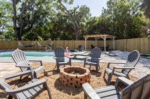 An outdoor seating area with Adirondack chairs and a fire pit, surrounded by a wooden fence and trees. - Earthy Oasis: Private Pool, Putt Putt & Fire Pit (Largo)