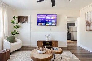 A living room with a flat-screen TV mounted on the wall, a white sofa, a wooden coffee table with a bowl, and a small side table. - Earthy Oasis: Private Pool, Putt Putt & Fire Pit (Largo)