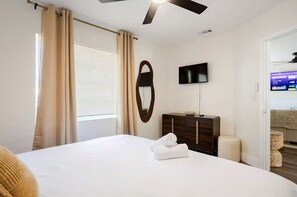 A hotel room with a bed, a flat-screen TV, a wooden dresser, and a window with curtains. - Earthy Oasis: Private Pool, Putt Putt & Fire Pit (Largo)