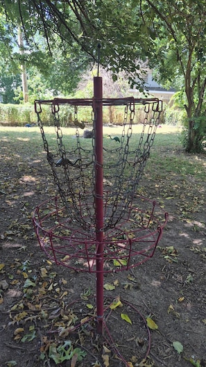 A disc golf basket with a chain-link fence, surrounded by trees and a grassy area.