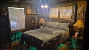 Una habitación con una cama, una mesita de noche, una lámpara y un ventanal con persianas.