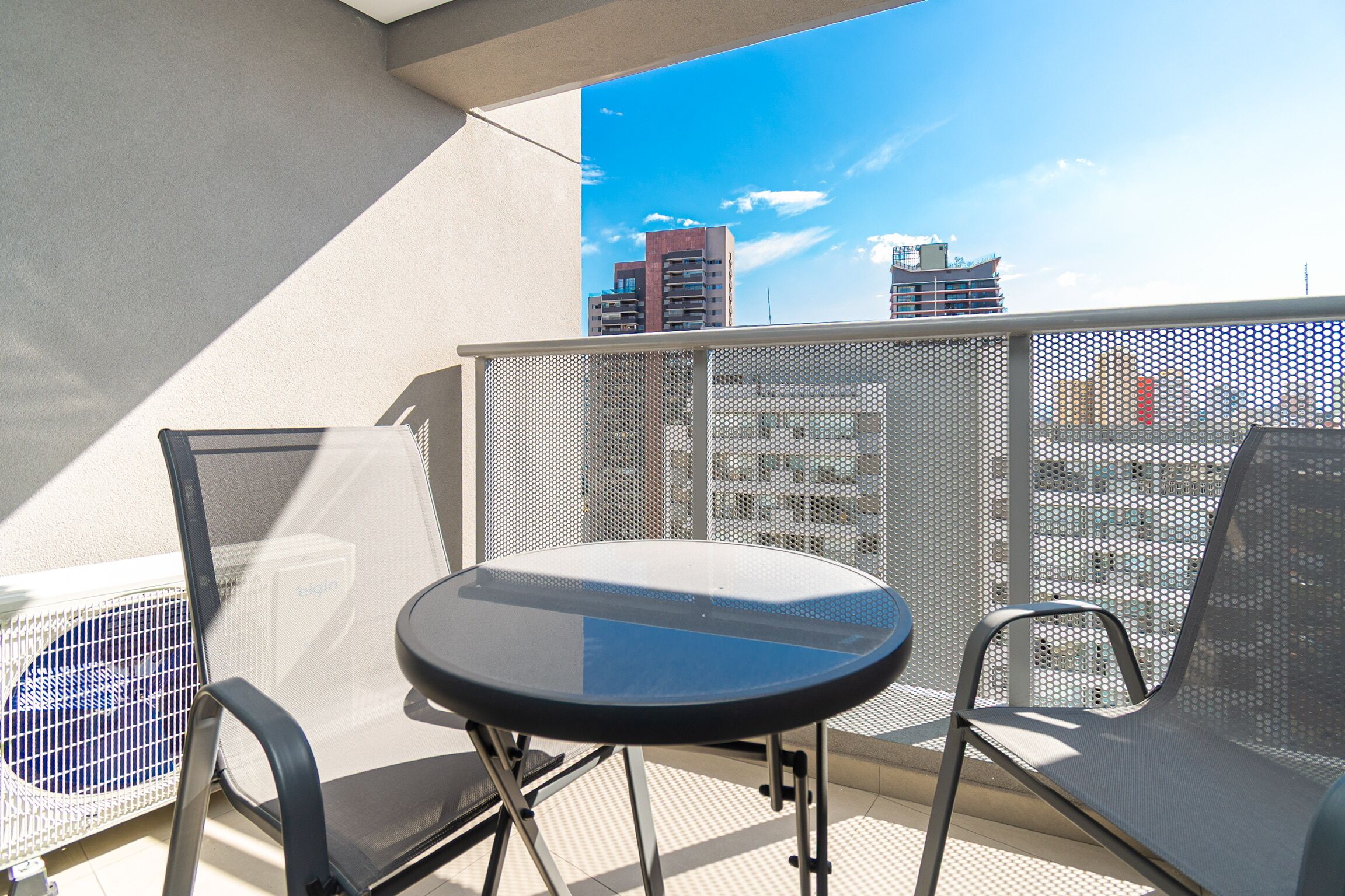 Un balcón con una mesa y dos sillas, con vistas a un paisaje urbano con edificios.