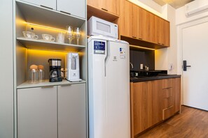 Cocina compacta con refrigerador, cafetera y microondas sobre la encimera.