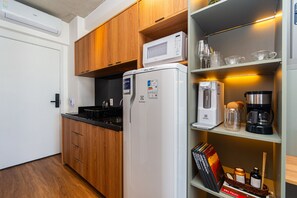 Cocina compacta con refrigerador, microondas, cafetera y un lavamanos pequeño.