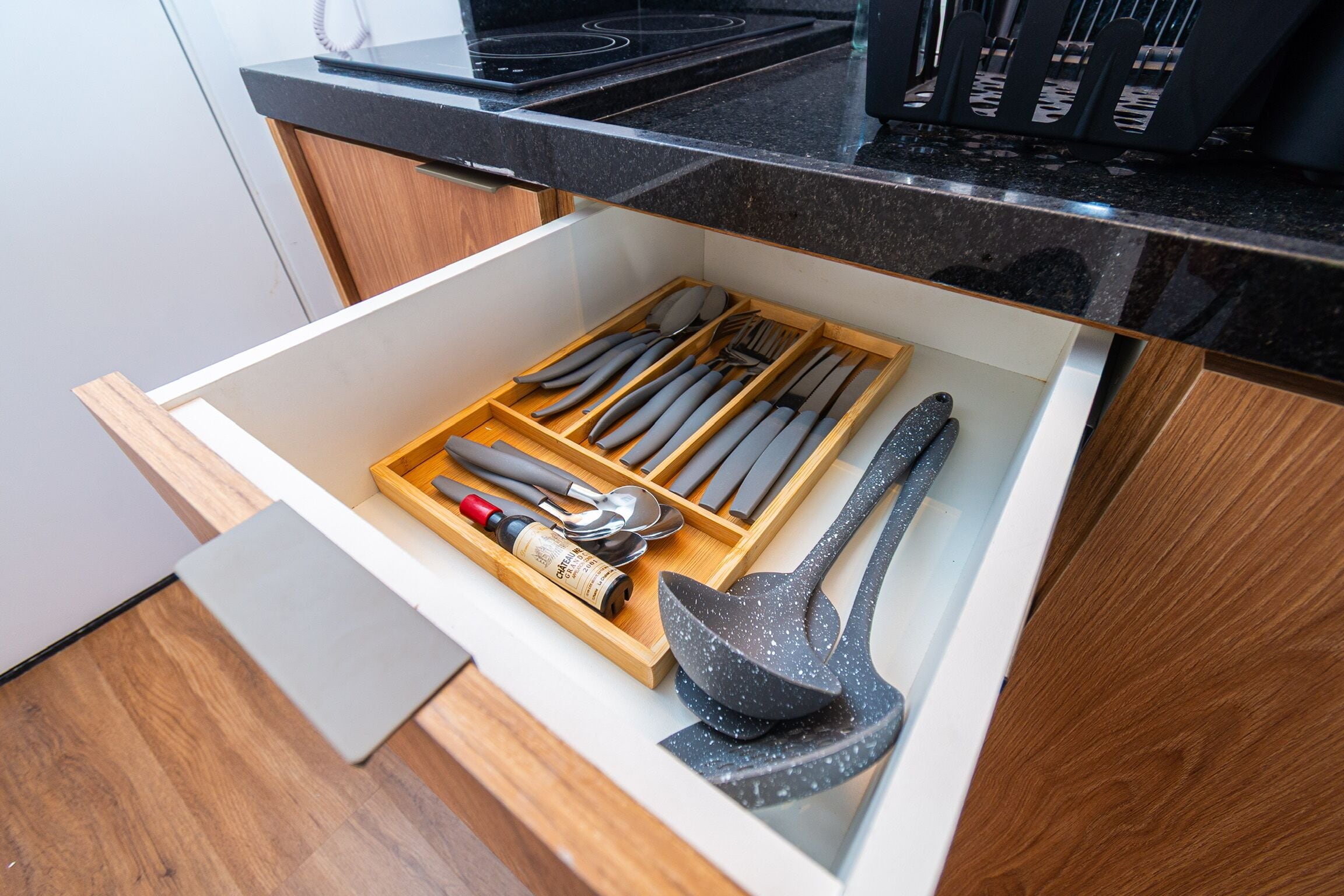 A drawer with kitchen utensils including a bottle, spoons, and a spatula.