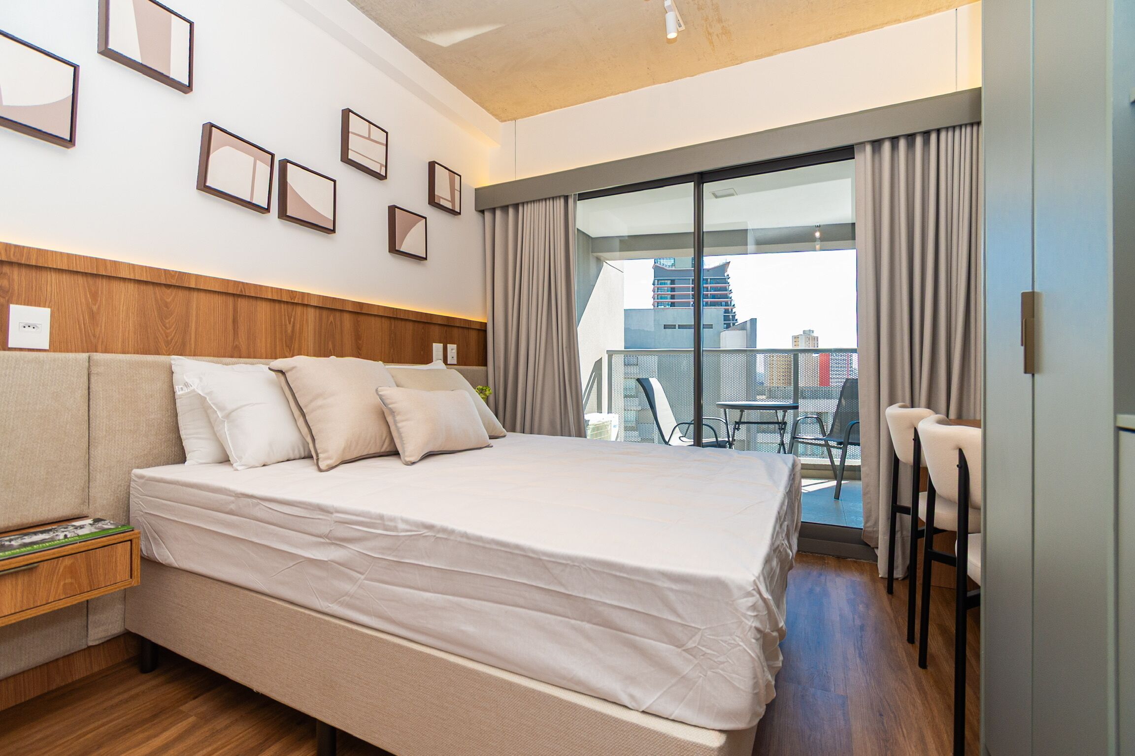 Quarto de hotel com cama, mesa de cabeceira, janela com cortinas e vista da cidade.
