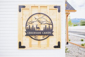 Ein hölzernes Schild mit Berg- und Baumkontur, beschriftet mit 'Creekside Cabins'.