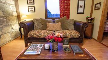 A cozy living room with a leather sofa, a coffee table with a magazine, a vase with flowers, and a window with curtains.