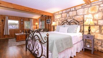 A bedroom with a stone wall, wooden beams, a bed with a headboard, bedside lamps, and a nightstand.