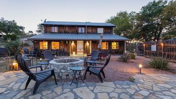 A rustic wooden building with a stone patio, outdoor seating, and a fire pit.