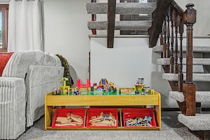 A room with a wooden play table, a red chair, and a staircase with a handrail.