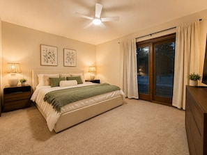 A bedroom with a bed, nightstands, a ceiling fan, and a view through a sliding glass door.