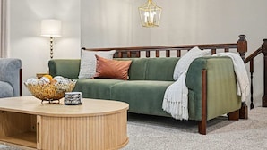 A green sofa with a white throw blanket, a wooden coffee table with decorative items, a floor lamp, and a hanging light fixture. - The Poolside farm house (Omaha)