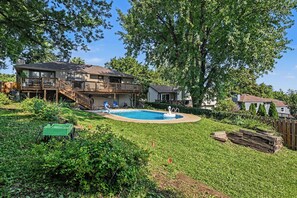 A residential backyard with a swimming pool, a wooden deck, and a fenced area.