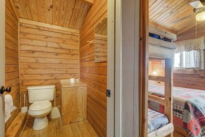 A wooden cabin interior with a wooden toilet, a small wooden cabinet, and a bed with a quilt. - Our Deluxe Cabin is great for families! (Buena Vista)