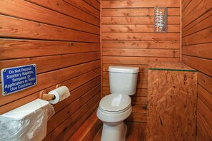 Ein Badezimmer im Stil einer Holzhütte mit Toilette, einer Toilettenpapierrolle und einem Schild, das darauf hinweist, keine Damenbinden, Tampons oder Applikatoren in die Toilette zu werfen.