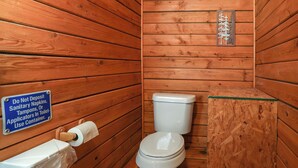 Ett badrum inrett som en enkel stuga, med en toalett, en toalettpappersrulle och en skylt som uppmanar att man inte ska slänga bindor, tamponger eller applikatorer i toaletten.