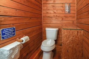Ein Badezimmer im Stil einer Holzhütte mit Toilette, einer Toilettenpapierrolle und einem Schild, das darauf hinweist, keine Damenbinden, Tampons oder Applikatoren in die Toilette zu werfen.