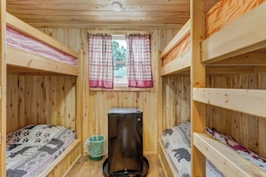 Eine Hütte mit Etagenbetten, einem Fenster mit Vorhängen und einem kleinen Kühlschrank.