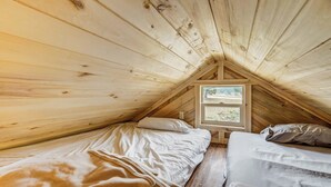 A small attic bedroom with two beds, wooden walls, and a window providing a view of the outdoors. - Our Cabin is great for youth groups, reunions and families! (Buena Vista)