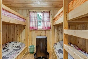 Eine Hütte mit Etagenbetten, einem Fenster mit Vorhängen und einem kleinen Kühlschrank.