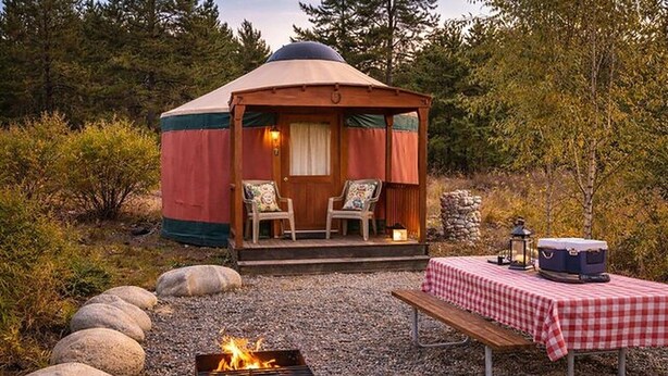 Una yurt con un focolare e un tavolo da picnic, circondata da rocce e alberi.