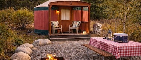 A yurt with a fire pit and picnic table, surrounded by rocks and trees.