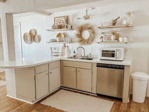 A kitchen with white cabinets, a microwave, and a sink. There are decorative items on shelves above the counter. - Lake Huron Cottage| Beach, Firepit + Sauna Retreat (Cheboygan)