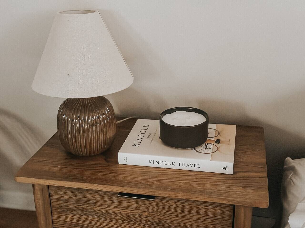 Une table de chevet avec une lampe, une bougie et un livre intitulé « KINFOLK TRAVEL ».