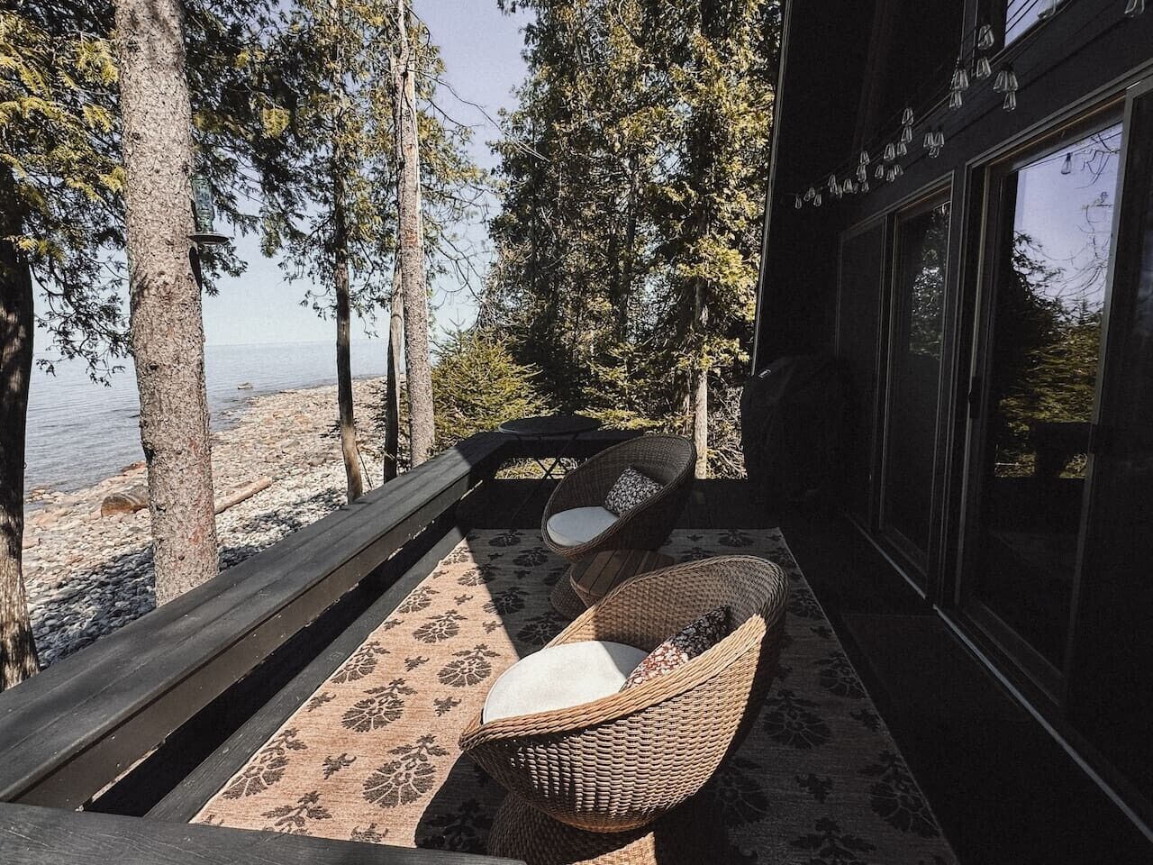 Un balcon avec des fauteuils et une table en osier, donnant sur une plage et des arbres.