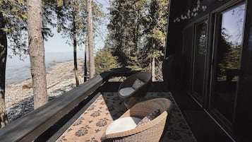 Un balcon avec des fauteuils et une table en osier, donnant sur une plage et des arbres.