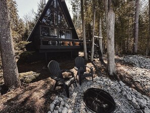 A cabin with a deck, two Adirondack chairs, and a fire pit.