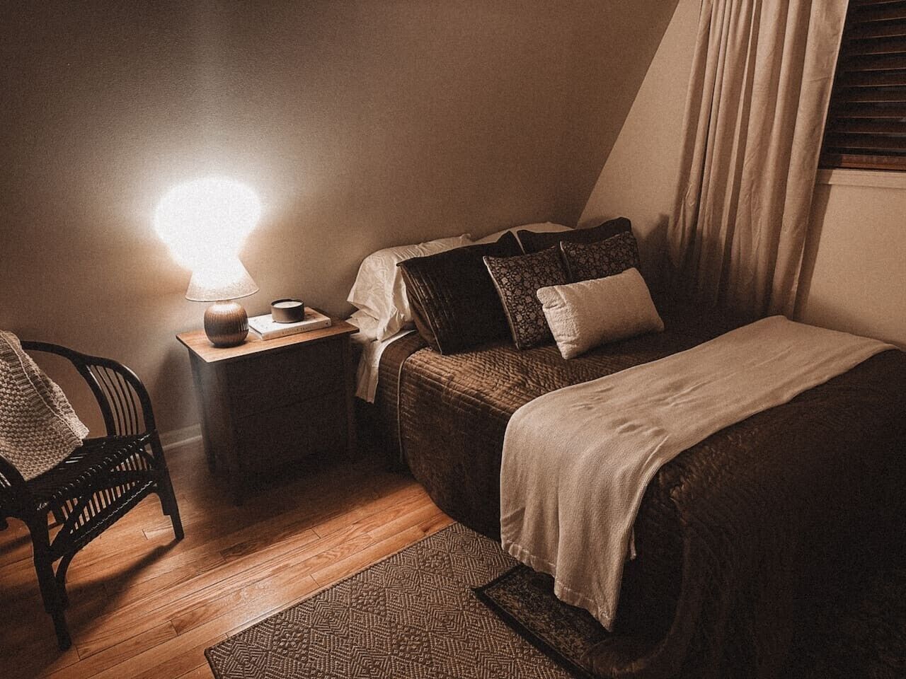 A cozy bedroom with a single bed, a bedside table with a lamp, and a chair.