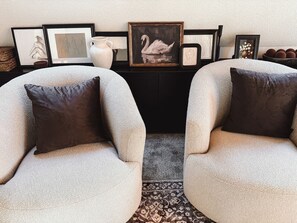 Two armchairs with dark cushions, a black side table with framed artwork, and a patterned rug.